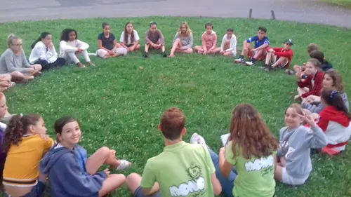 Assis en ronde dans un champ, des enfants savourent leur colo d'été 2022